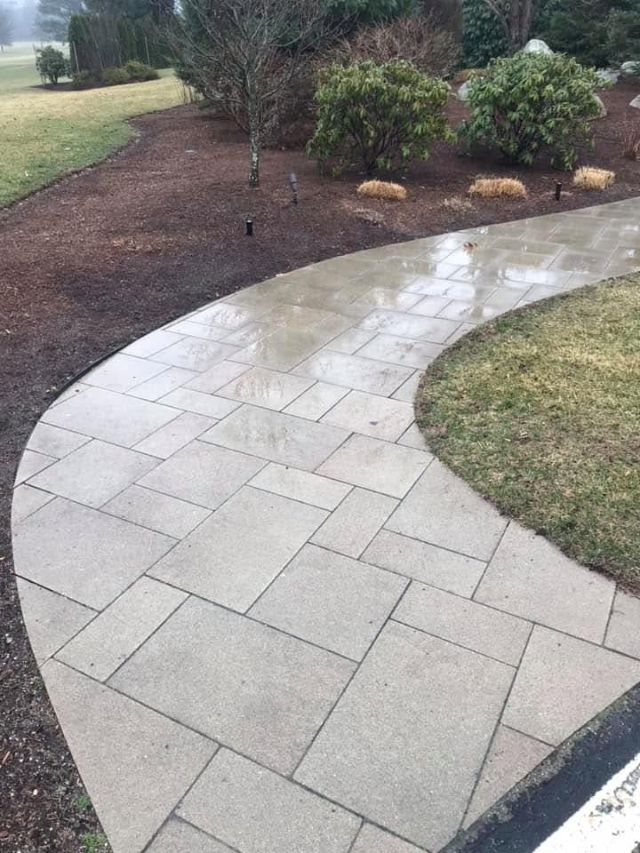 Wet bluestone-toned paver walkway curving through mulched planting beds toward open lawn