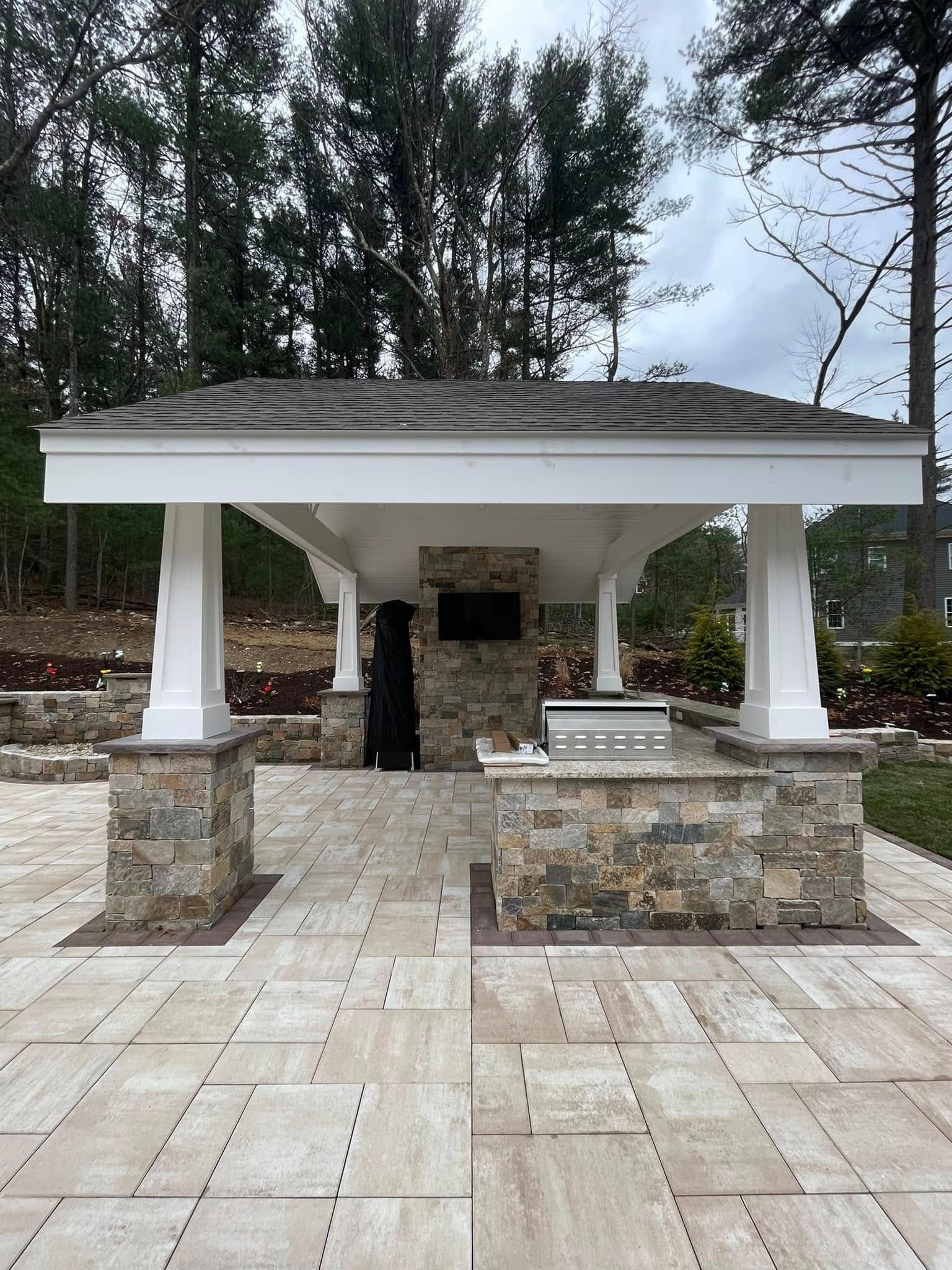 Covered outdoor kitchen pavilion with natural stone veneer piers and a large-format porcelain paver terrace