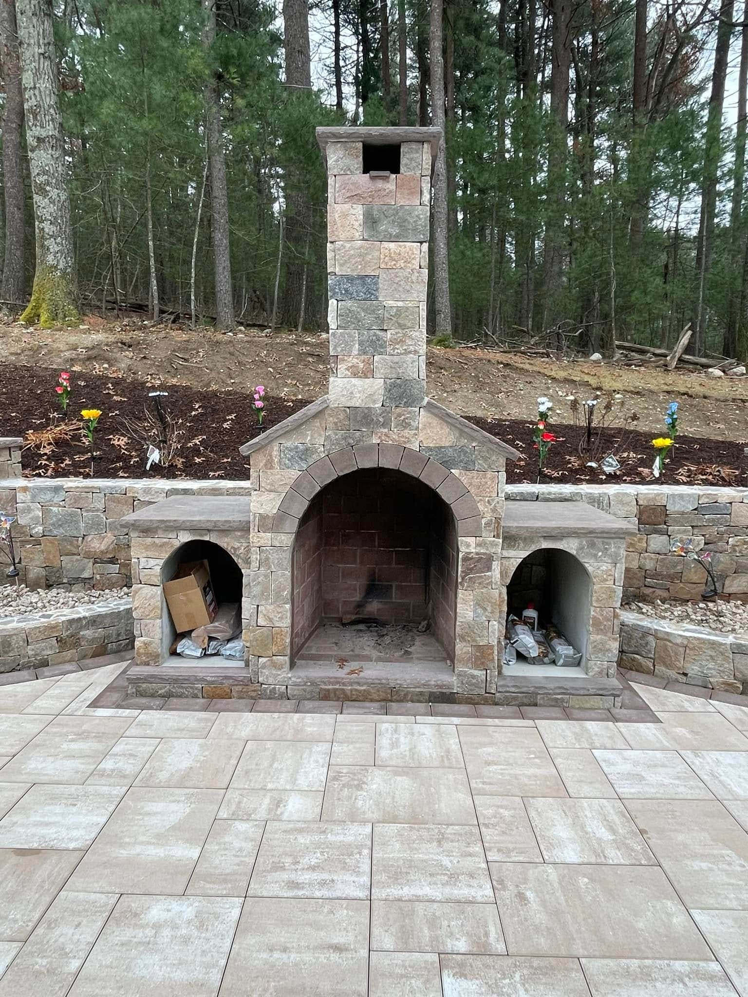 Natural stone outdoor fireplace with an arched firebox and flanking wood-storage arches, set into a stone seat wall