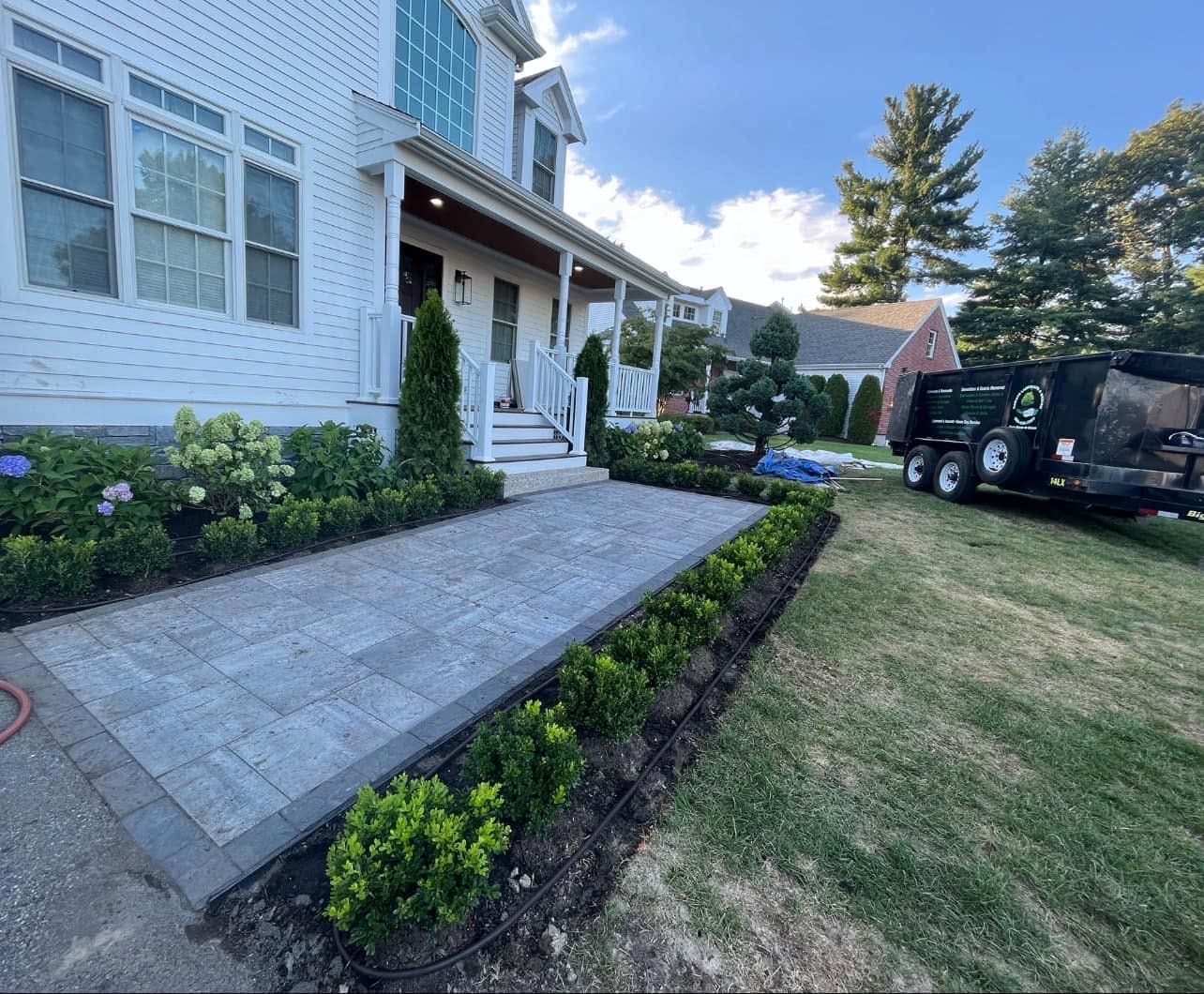 Wide paver front walk to a white farmhouse porch, flanked by new boxwood hedging and hydrangea