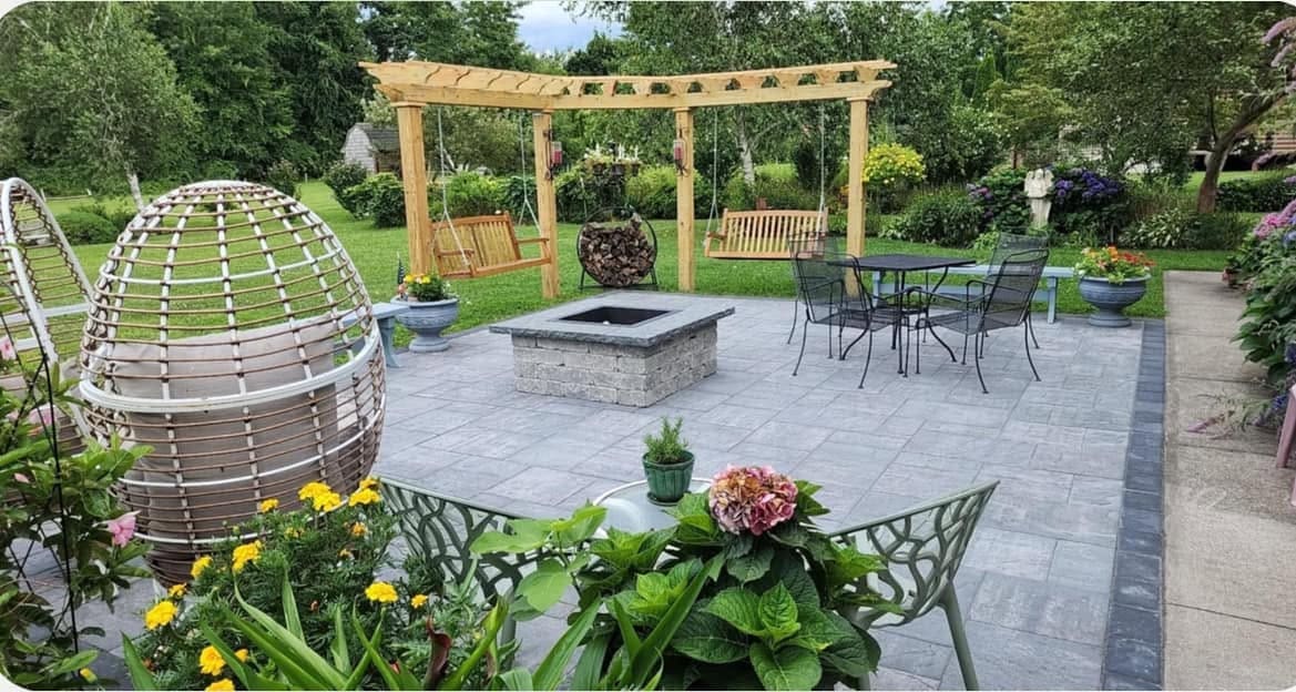 Grey paver terrace with a square gas fire table, cedar swing pergola and a charcoal soldier-course border