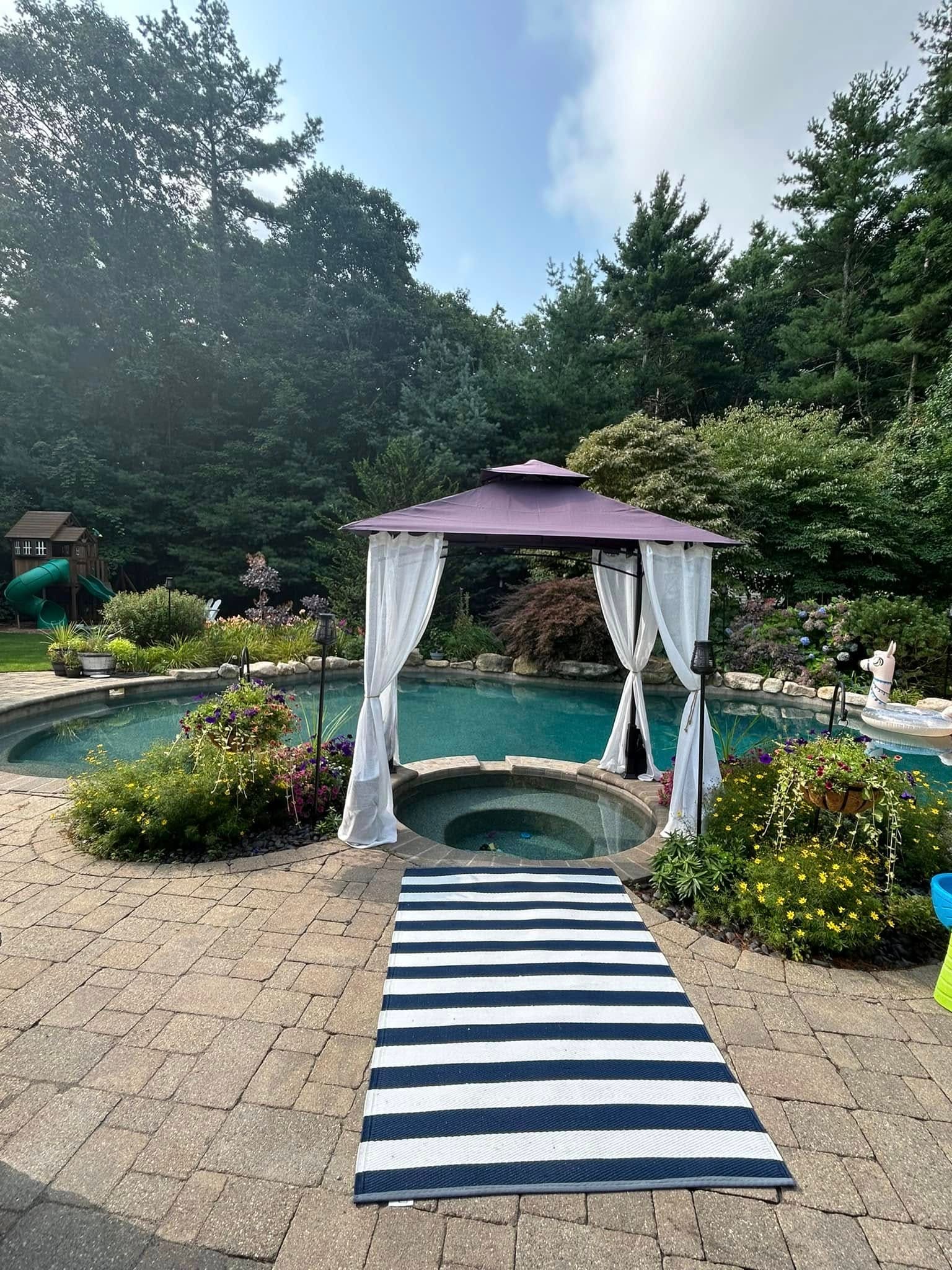 Paver pool surround with a raised spa, boulder coping and deep perennial borders under a shade canopy
