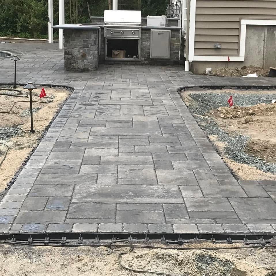 Paver terrace laid to the outdoor kitchen with edge restraint exposed and the pool excavation still open alongside