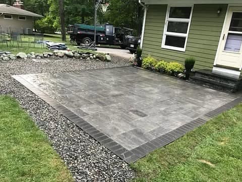 Rear paver patio with a charcoal soldier-course border and a washed-stone drainage margin along the foundation