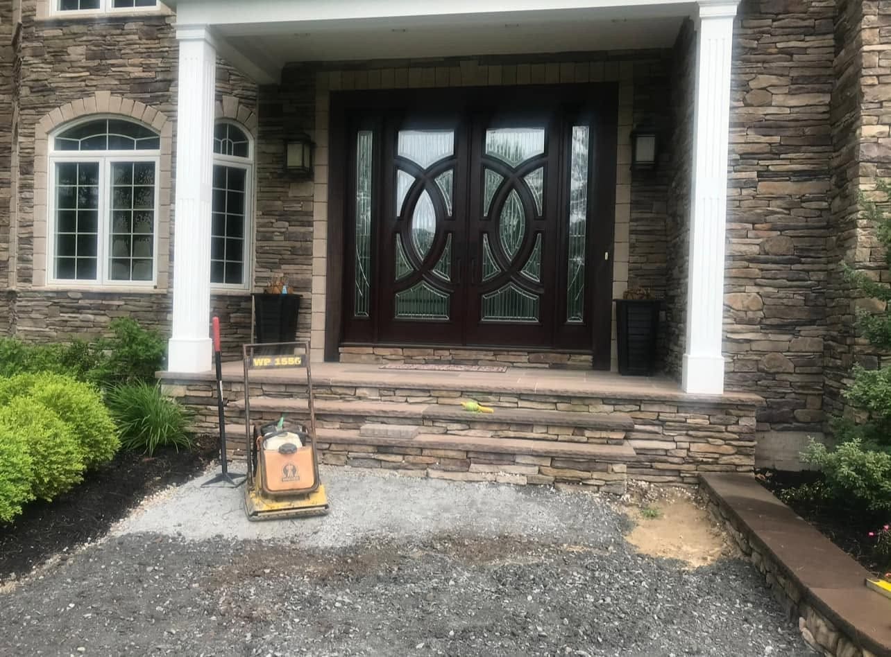 Plate compactor on the processed-gravel base in front of newly set stone entry steps, mid-installation
