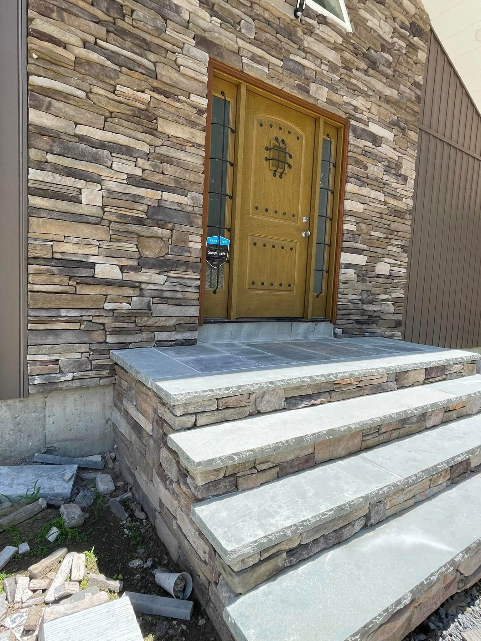 Stone entry steps with dry-stack veneer risers and full-thickness stone treads, landing tiled and cutting debris still on the ground